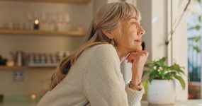 Window, smile and elderly woman with thinking at home for retirement, satisfaction and peace on weekend. Relax, senior person and calm with idea for reflection, mindfulness and good memory in house
