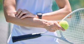 Sports, arm pain and tennis player with a racket and ball standing on a court during for a match. Closeup of a health, strong and professional athlete with equipment touching a medical elbow injury.