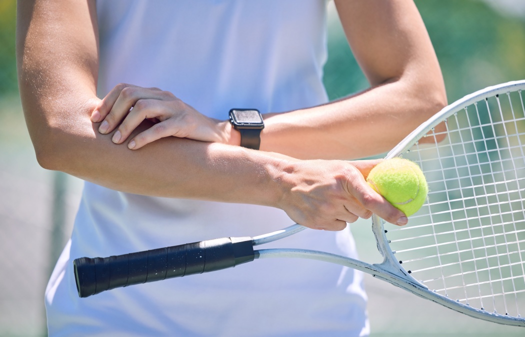 Sports, arm pain and tennis player with a racket and ball standing on a court during for a match. Closeup of a health, strong and professional athlete with equipment touching a medical elbow injury.