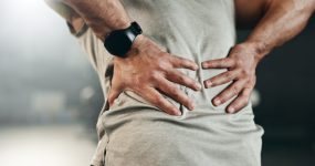 Fitness, back pain and hands of man at gym for training with muscle, problem or arthritis. Sports, injury and guy athlete with joint massage for backache, fibromyalgia or osteoporosis accident.